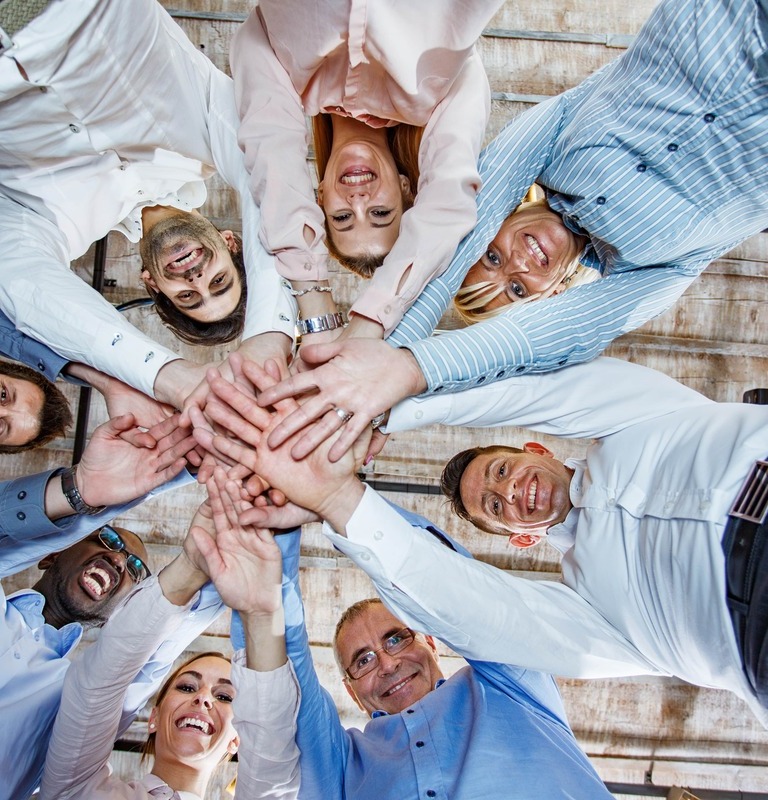 Low angle view of a large group of happy entrepreneurs joining their hands in unity and looking at the camera.