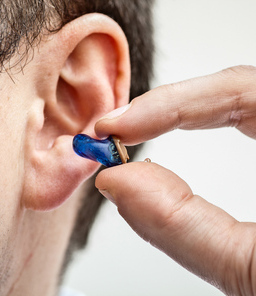 In-the-ear hearing aid held between two fingers is being inserted into an ear.