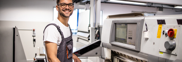 A factory worker smiling cheerfully while standing in front of a machine.