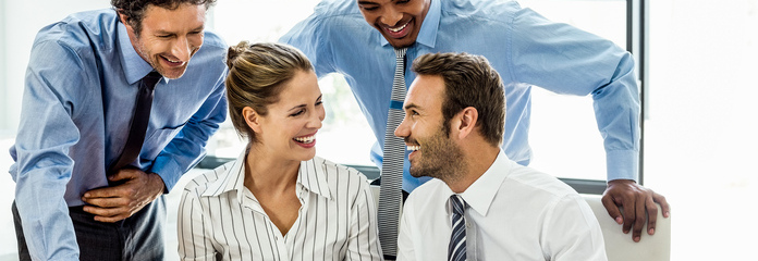 A group of smiling individuals gathered around a computer, engaged in a lively discussion.