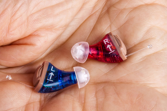 Two in-the-ear hearing aids in the palm of a hand.