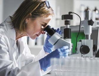 A woman inspecting the quality of a PCB using a microscope.